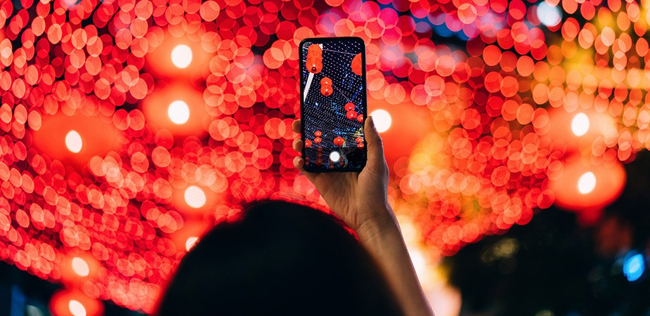 Woman holding cell phone with clear picture of the out of focus colorful city scene in front of her.