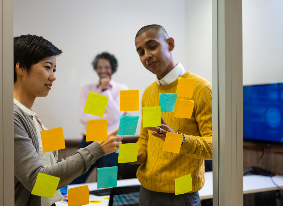 woman and man in the office placing post-it notes on a clear board