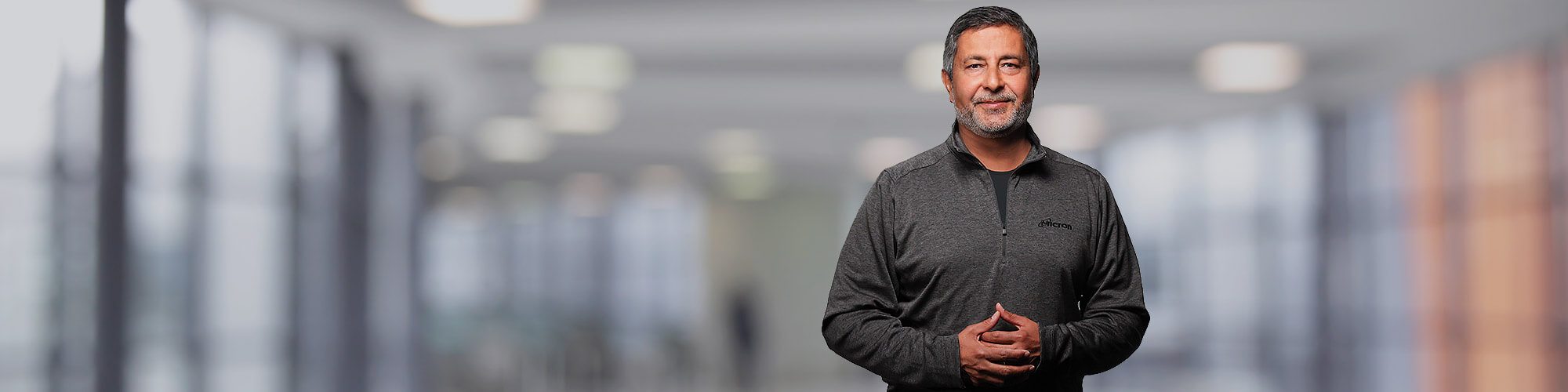 Sanjay in Micron branded quarter zip standing in blurred hallway background